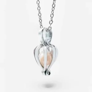 Silver necklace with cage-style heart pendant holding a soft pink pearl, suspended on a delicate chain against a white background