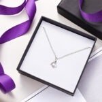 Delicate silver necklace with small crystal pendant displayed in a gift box with purple ribbon, elegant jewelry gift presentation