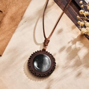 Handcrafted wooden moon phase pendant necklace with round black resin inlay and braided cord on a neutral background
