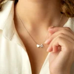 A close-up of a woman wearing a delicate silver necklace with a small heart charm and the letter "M," resting just below the collarbone