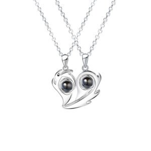A pair of silver matching pendant necklaces, each featuring a black projection element within a swirl design, forming a complementary heart shape when placed side by side.
