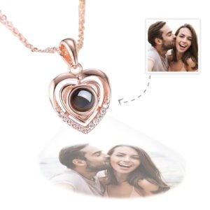 Personalized heart-shaped pendant necklace in rose gold with black projection sphere, displaying a photo of a smiling couple. The necklace features small crystals along the outer heart frame and is shown with a matching chain, highlighting the unique projection feature that casts the photo below the pendant