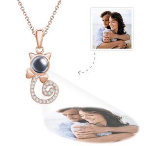 A rose gold cat-shaped pendant necklace featuring a central black projection element, a curled tail encrusted with small crystals, and customizable engraved photo projected below showing a couple embracing by the seaside.