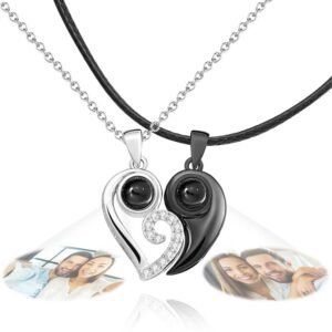 A pair of heart-shaped projection necklaces forming a yin-yang design, one in silver and one in black, each projecting a custom photo of a smiling couple, symbolizing love and connection.
