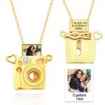 Gold camera-shaped pendant necklace with a small photo slot at the top, heart-shaped accents, and a gold chain. Shows front view with a sample photo inserted and back view with custom engraved text, personalised keepsake jewelry