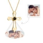 A gold cross-shaped pendant necklace with a projection feature in the center, displaying a customizable engraved photo below the pendant of a couple smiling and leaning foreheads together