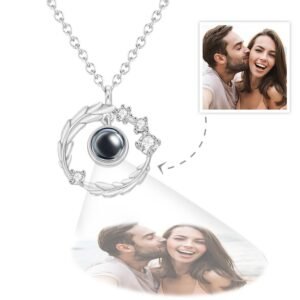 A silver circular pendant necklace featuring a central black projection element surrounded by small crystals, displaying a customizable engraved photo below the pendant of a couple smiling and laughing together.