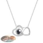 Personalized double heart projection necklace in silver, featuring one heart with small crystals and a black projection bead, projecting a photo of a smiling couple in a romantic pose.