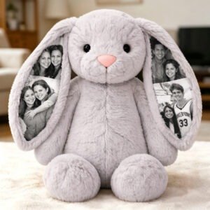Personalized plush bunny with long floppy ears featuring four black-and-white photo prints of happy people, sitting on a cream-colored carpet in a cozy living room.