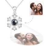 A silver flower-shaped pendant necklace featuring a central black gem and six surrounding heart-shaped crystals, with a customizable photo engraved below the pendant showing a couple smiling and laughing.
