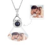 A silver pendant necklace with an elegant looped design and a central black projection, featuring a customizable engraved photo below the pendant of a couple leaning foreheads together and smiling.