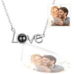 Personalized 'Love' necklace with a silver chain, featuring a projection pendant that displays a couple's photo. The necklace is shown with the photo projected below and a small inset of the original couple image in the top right corner.
