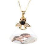 Custom projection necklace in gold shaped like an angel with sparkling wings, projecting a photo of a couple embracing outdoors.