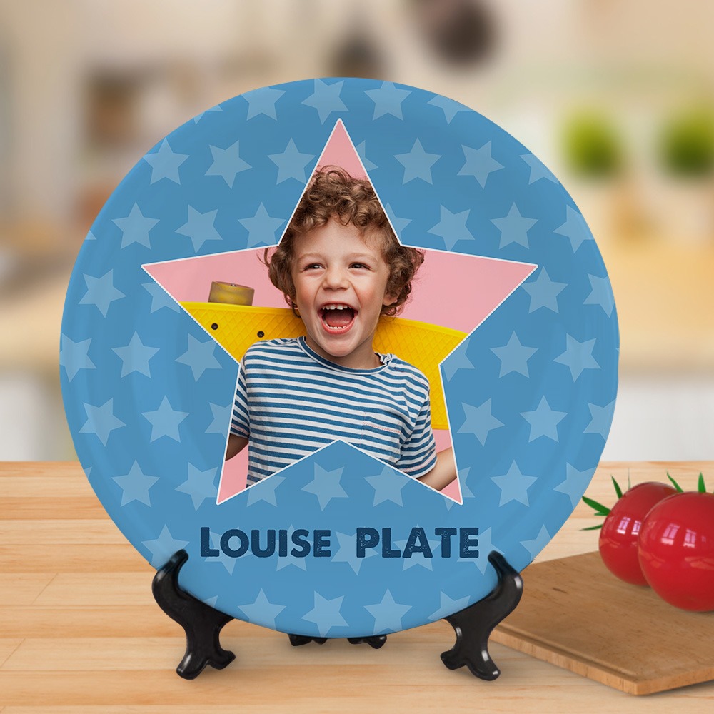 9dad74f7-a5fb-4535-bfb6-d85608423f4a-0jpeg - Printshop4me.au Personalized blue round kids plate with a star-pattern background and a large star-shaped cutout in the center featuring a smiling child laughing. The bottom of the plate is labeled “LOUISE PLATE,” and it is displayed on a wooden tabletop with a stand, creating a playful custom gift presentation.