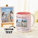 Personalized ceramic mug with a pink gradient interior featuring the text “Friends Forever” and a photo of two friends holding hands on a beach. The mug includes custom text reading “CA & CHARLOTTE, HAWAII, AUGUST 2023.” In the background, a framed photo of the same scene is displayed on a small wooden easel, with a “CUSTOM TEXT” label pointing toward the personalization area.