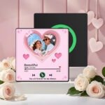 Personalized pink custom photo music plaque featuring a couple inside a layered heart-shaped frame with floating heart icons and sparkles. The design displays the song “Beautiful” by Giulio Cercato in a Spotify-style music player layout with playback controls, progress bar, and a short romantic caption reading “You will forever be my always.” The plaque is displayed in a romantic setup with white roses and a soft pink decorative background, with a second black display panel behind it.
