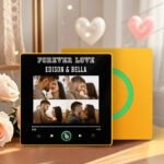 Personalized custom photo music plaque titled “FOREVER LOVE – EDISON & BELLA” featuring a collage of romantic couple photos arranged in a grid. The design appears on a black Spotify-style music interface with playback controls, progress bar, and a green circular record element. The plaque has a yellow border and is displayed in a warm indoor setting with decorative heart ornaments and soft floral accents.