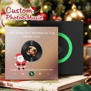 Personalized photo and music acrylic plaque featuring a custom couple photo embedded in a vinyl record design, displayed with the song "All I Want for Christmas Is You" by Mariah Carey. The festive Christmas-themed plaque includes a Santa illustration, music player controls, and a Spotify-style code, set against a blurred holiday background with Christmas tree decorations and warm lights.