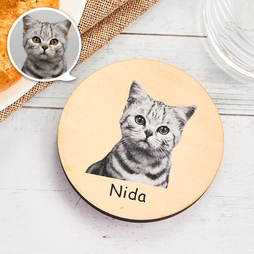 CCD077jpg - Printshop4me.au Round wooden personalized pet plaque featuring a grayscale portrait of a kitten printed in the center, with the name “Nida” written below. A small speech-bubble style inset shows a close-up of the cat’s face in the top-left corner. The plaque is placed on a light wooden surface with decorative table elements around it.