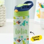 Personalized kids' stainless steel water bottle with a green and navy blue flip-top straw lid and carry handle, featuring a playful dinosaur-themed design with cartoon dinosaurs, pterodactyls, palm trees, and prehistoric plants. The bottle is customized with the name "Lulia" and displayed on a desk with a "Custom Name" label.