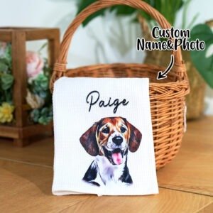 Personalized kitchen towel displayed in a wicker basket, featuring a colorful illustrated beagle dog portrait with the name “Paige” printed above. The towel is placed on a wooden surface with a cozy home décor background.