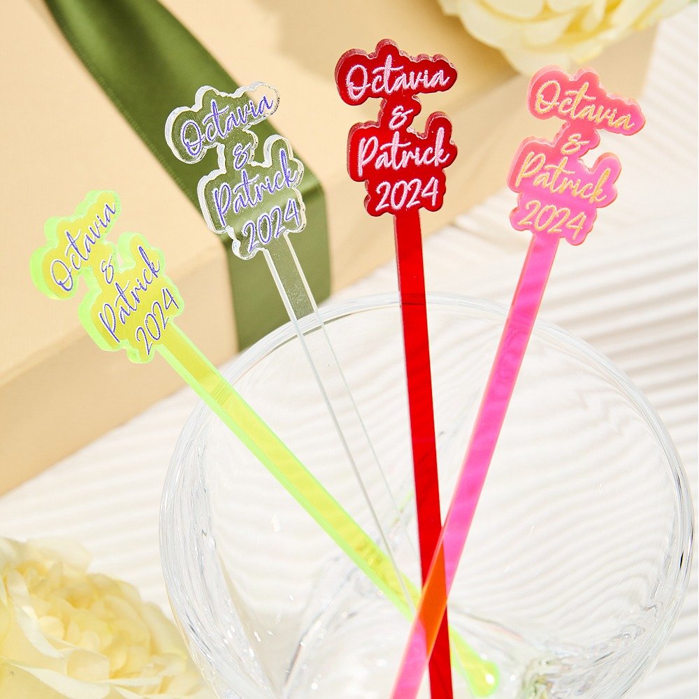 a9c3fa9f-3c64-43fc-ad44-1f84228f8224-0jpeg - Printshop4me.au Colorful personalized drink stirrers placed in a glass bowl, featuring names “Octavia & Patrick 2024” in different styles and colors including red, pink, neon green, and silver. The sticks are arranged like party decorations, suggesting custom wedding or celebration drink accessories.