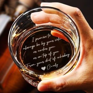 Close-up of a hand holding a glass of whiskey, viewed from above, with engraved handwritten-style text inside the glass reading a romantic message: “I promise to always be by your side, or under you, or on top of you… From your shot of whiskey Candy,” making it a personalized gift drinkware item.