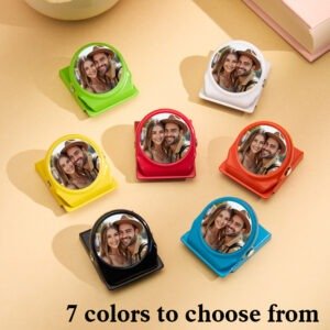 A set of custom photo fridge magnets displayed in multiple bright colors (green, white, red, yellow, black, and blue), each featuring a circular couple portrait. The magnets are arranged neatly on a warm beige surface with the text “7 colors to choose from” at the bottom, showcasing personalization and product